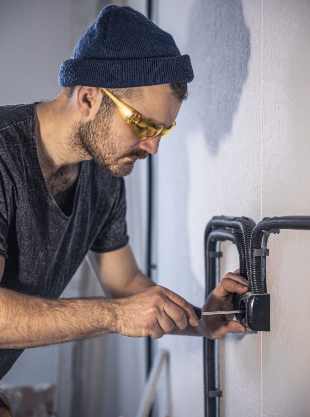 Attractive male electrician repairing an outlet, installing an outlet indoors.
